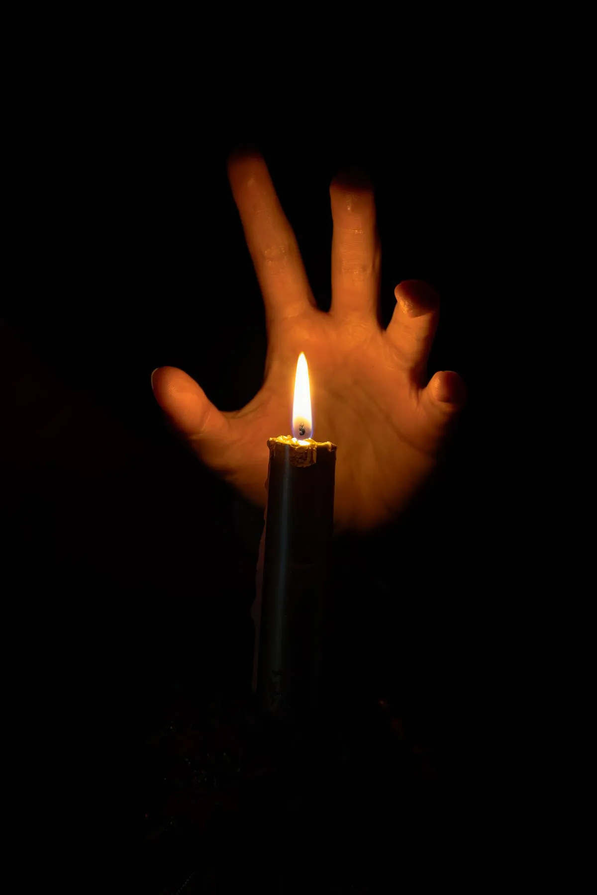 A hand reaching toward a candle flame glowing in the darkness