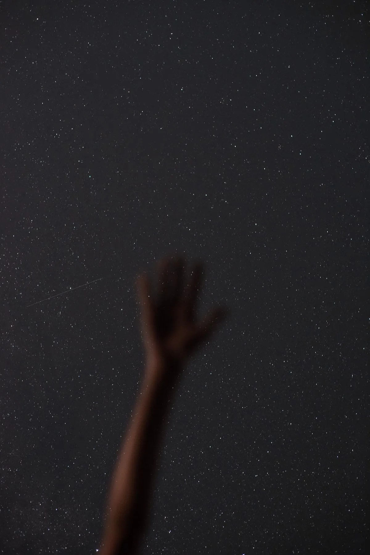 A hand reaching toward a vast, star-filled night sky
