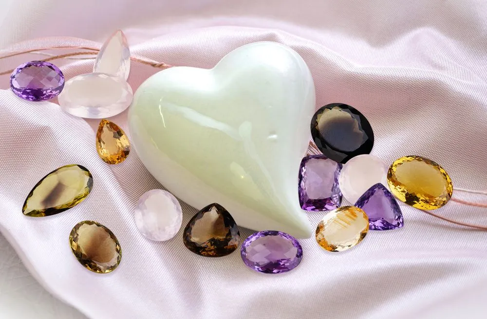 A heart-shaped crystal surrounded by colorful gems on pink silk fabric