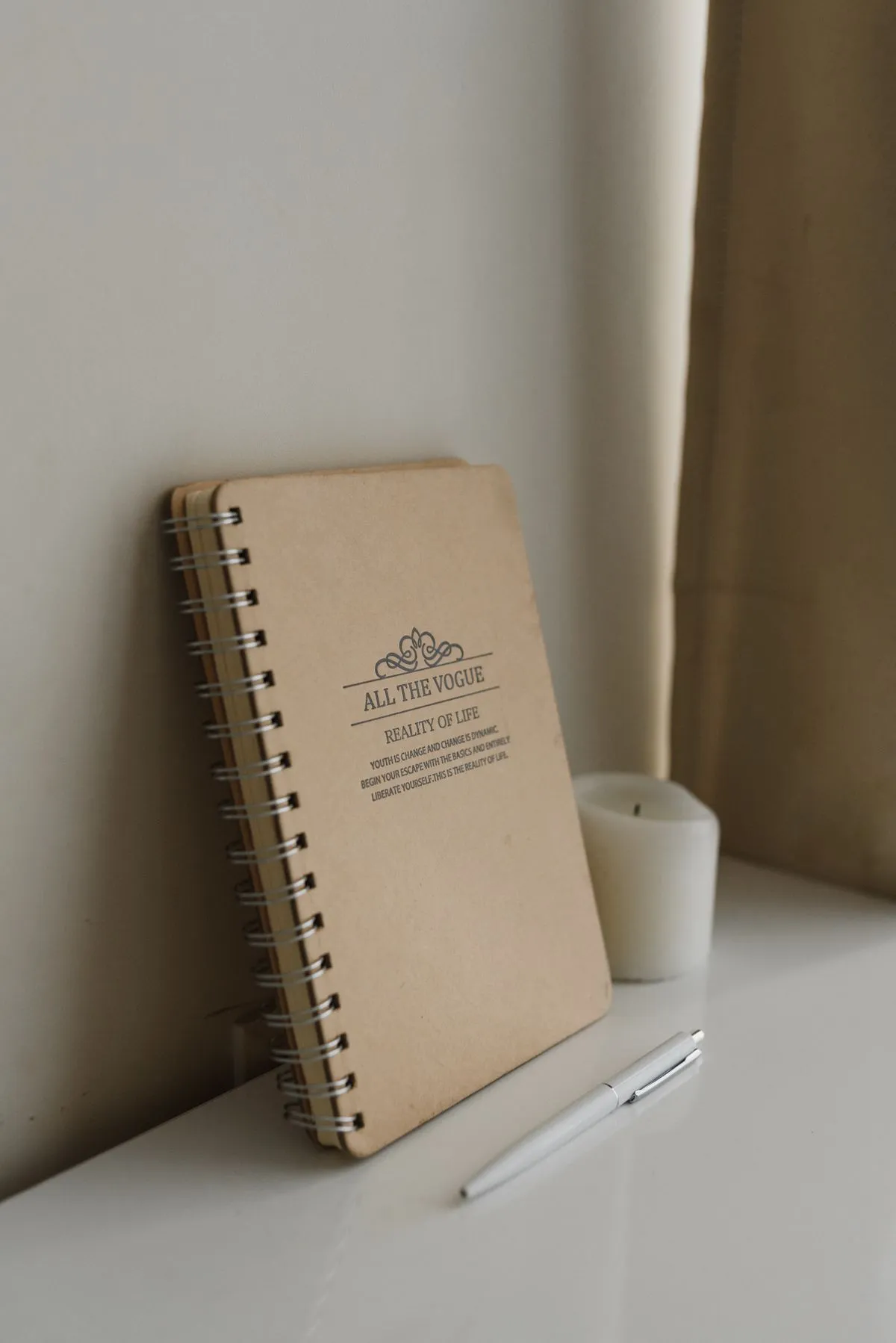 An open notebook, pen, and lit candle arranged on a desk