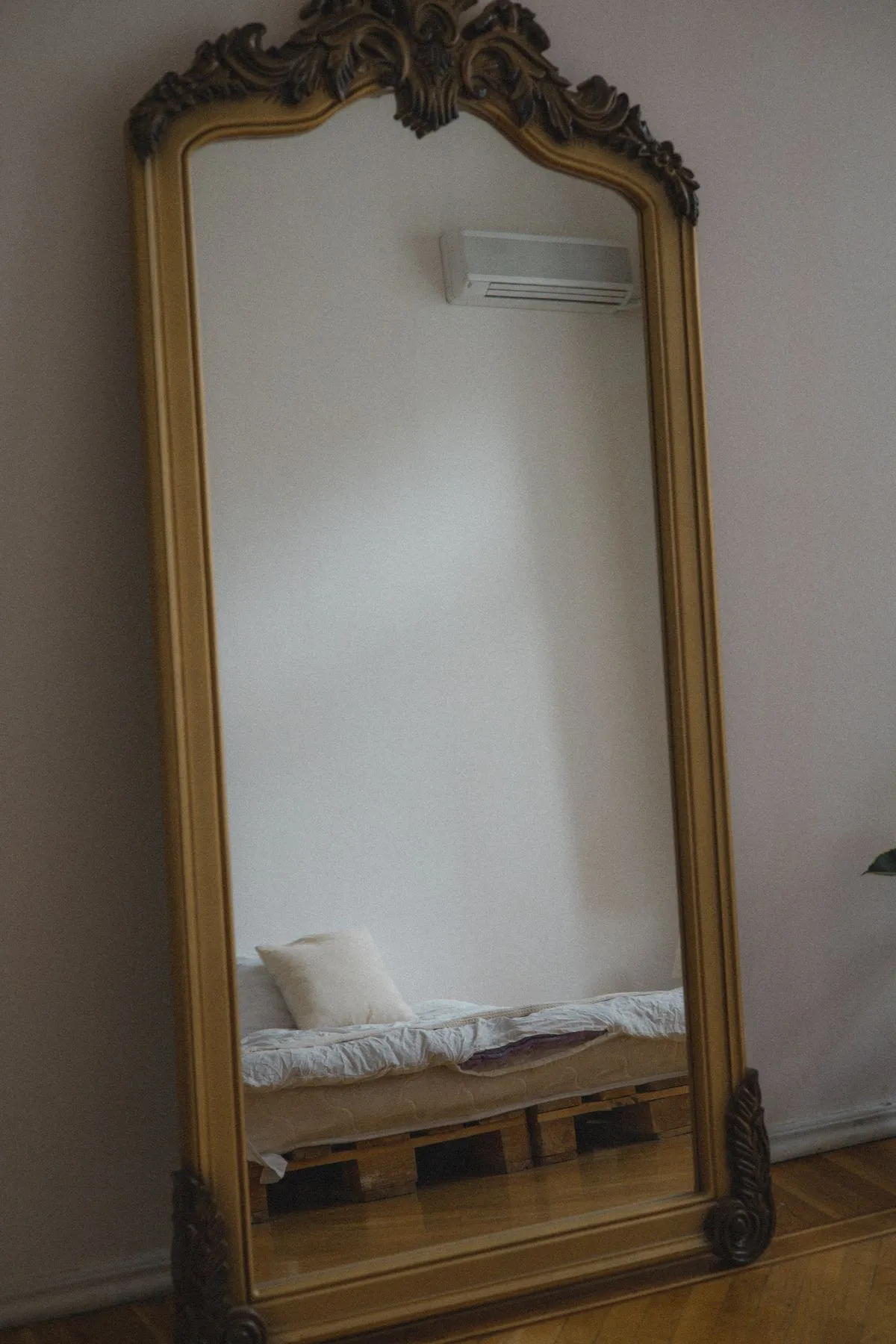 A large ornate mirror reflecting a minimalist bedroom with a bed