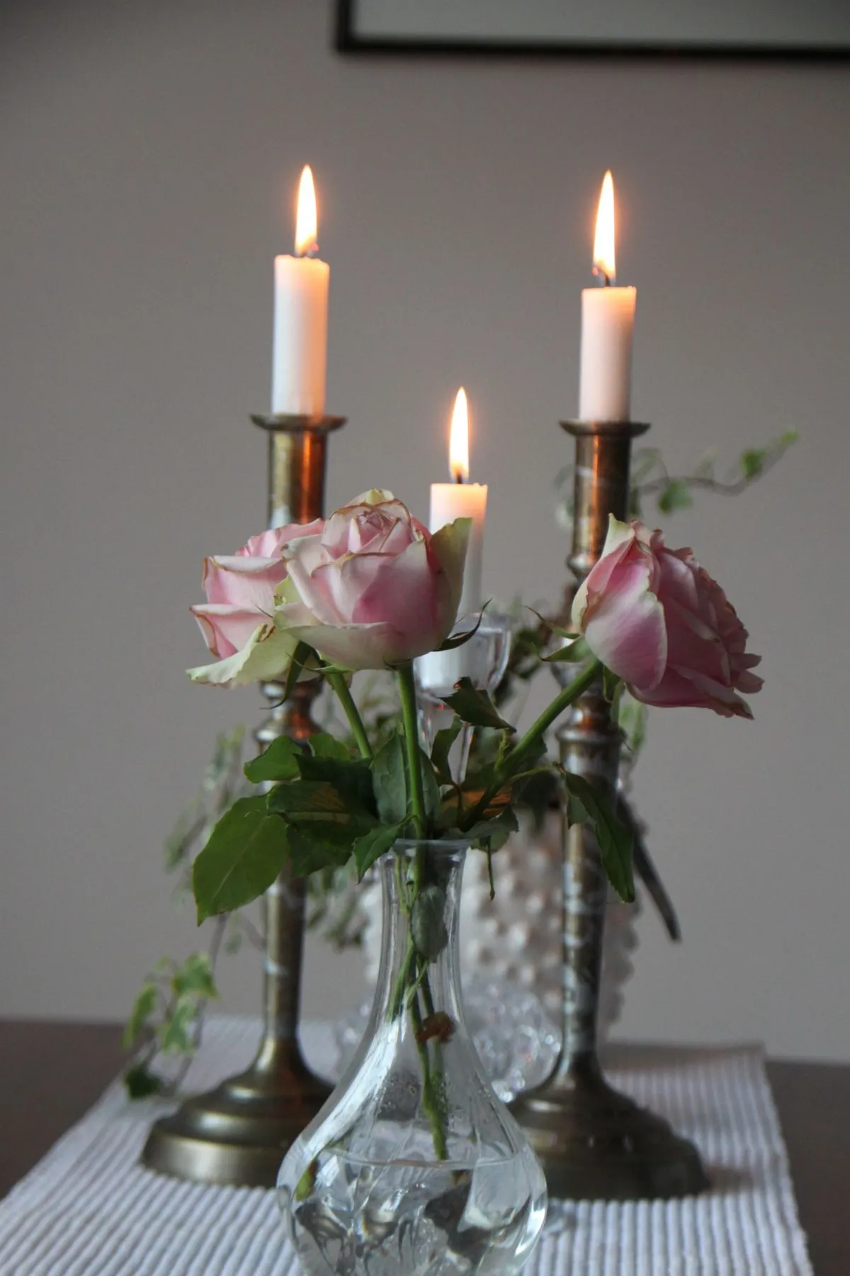 Pink roses arranged in a vase beside lit candles