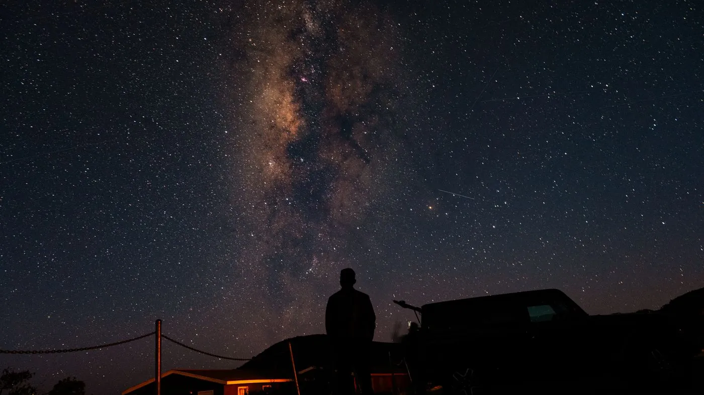 Silhouette of a person standing beneath a sky full of stars and the Milky Way