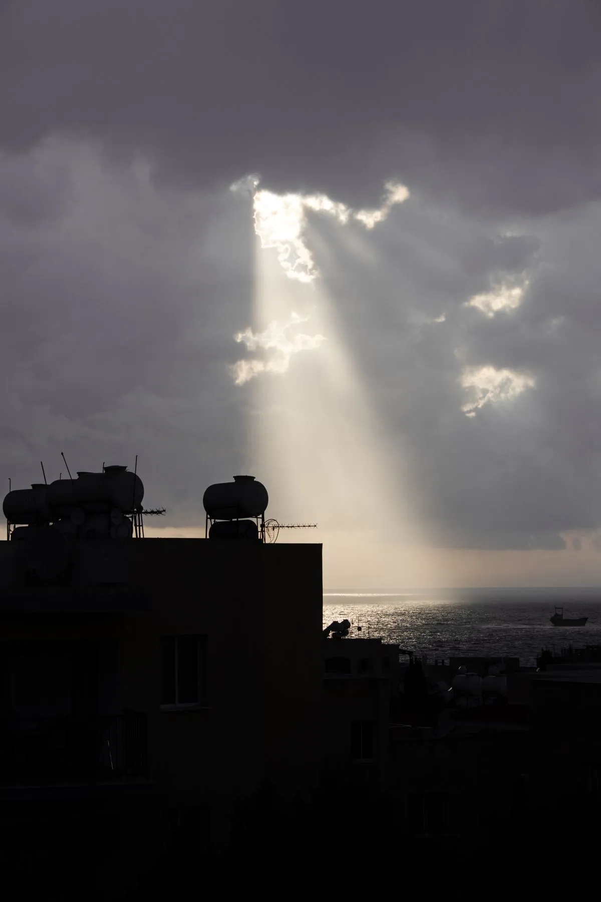Sunbeams piercing through dramatic storm clouds over a coastal skyline